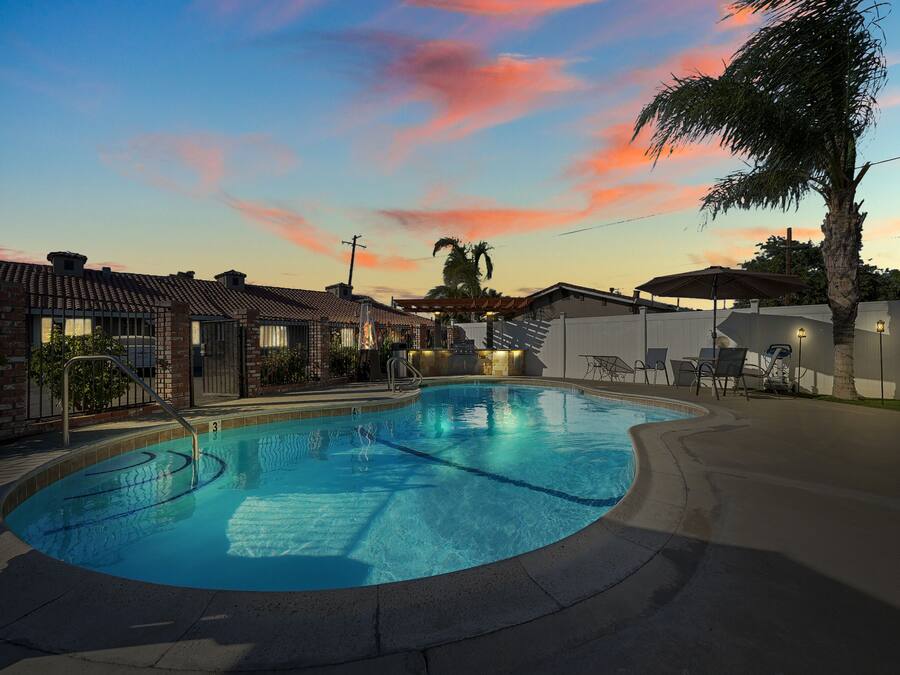 A swimming pool with a curved edge, surrounded by a patio area with chairs and tables.