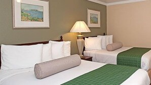 A hotel room with two beds, a nightstand, a lamp, and framed artwork on the walls. - Traveler's Inn (Williams)