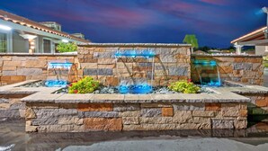A stone fountain with water features, surrounded by a stone wall and plants. - Traveler's Inn (Williams)