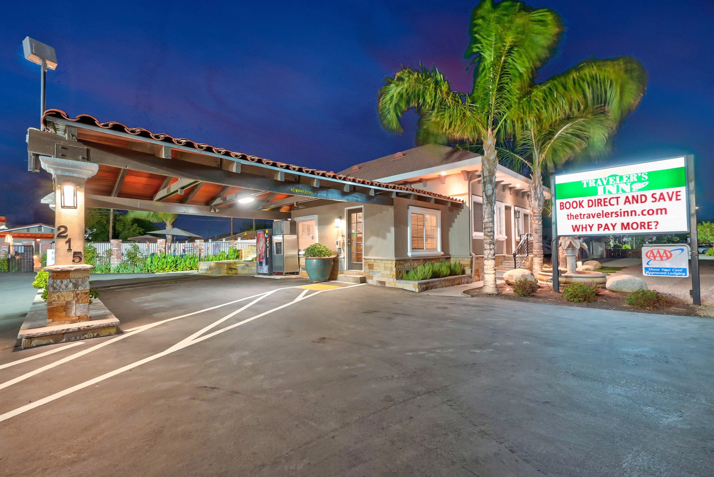 A hotel entrance with a covered parking area, palm trees, and a sign advertising direct booking with AAA.