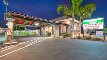 A hotel entrance with a covered parking area, palm trees, and a sign advertising direct booking with AAA.