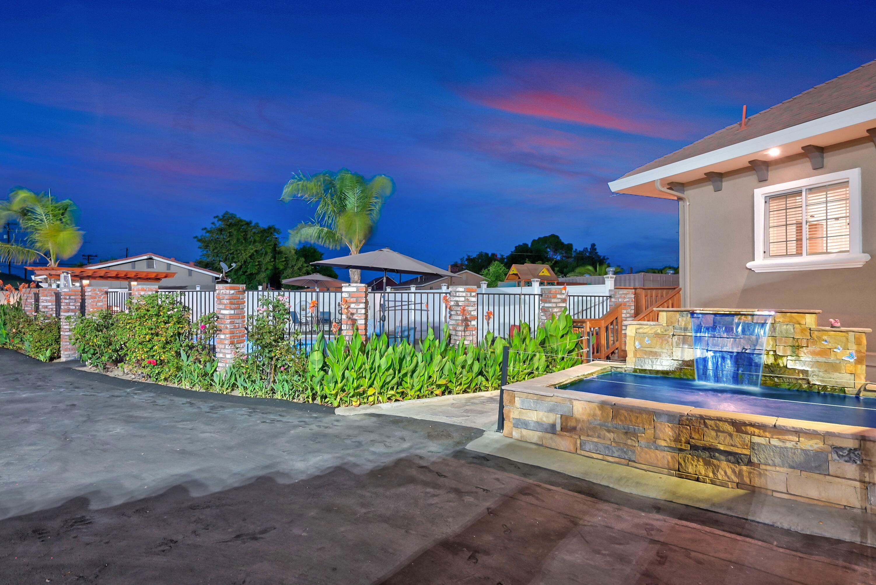 A residential property with a swimming pool, stone waterfall feature, and a well-maintained garden with palm trees.