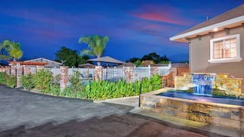 A residential property with a swimming pool, stone waterfall feature, and a well-maintained garden with palm trees.