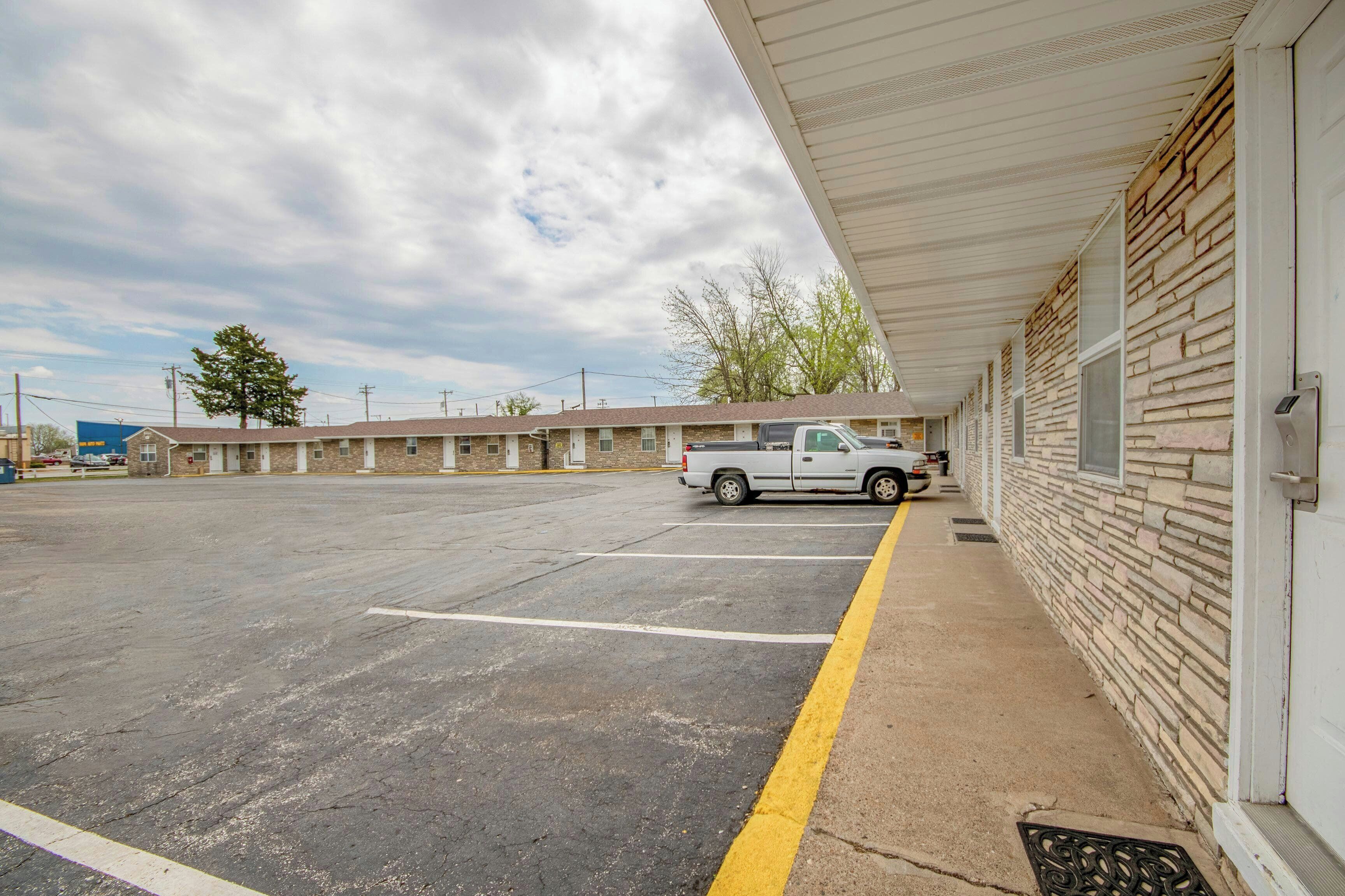 A motel with a parking lot, a white truck parked, and a row of rooms with brick walls.