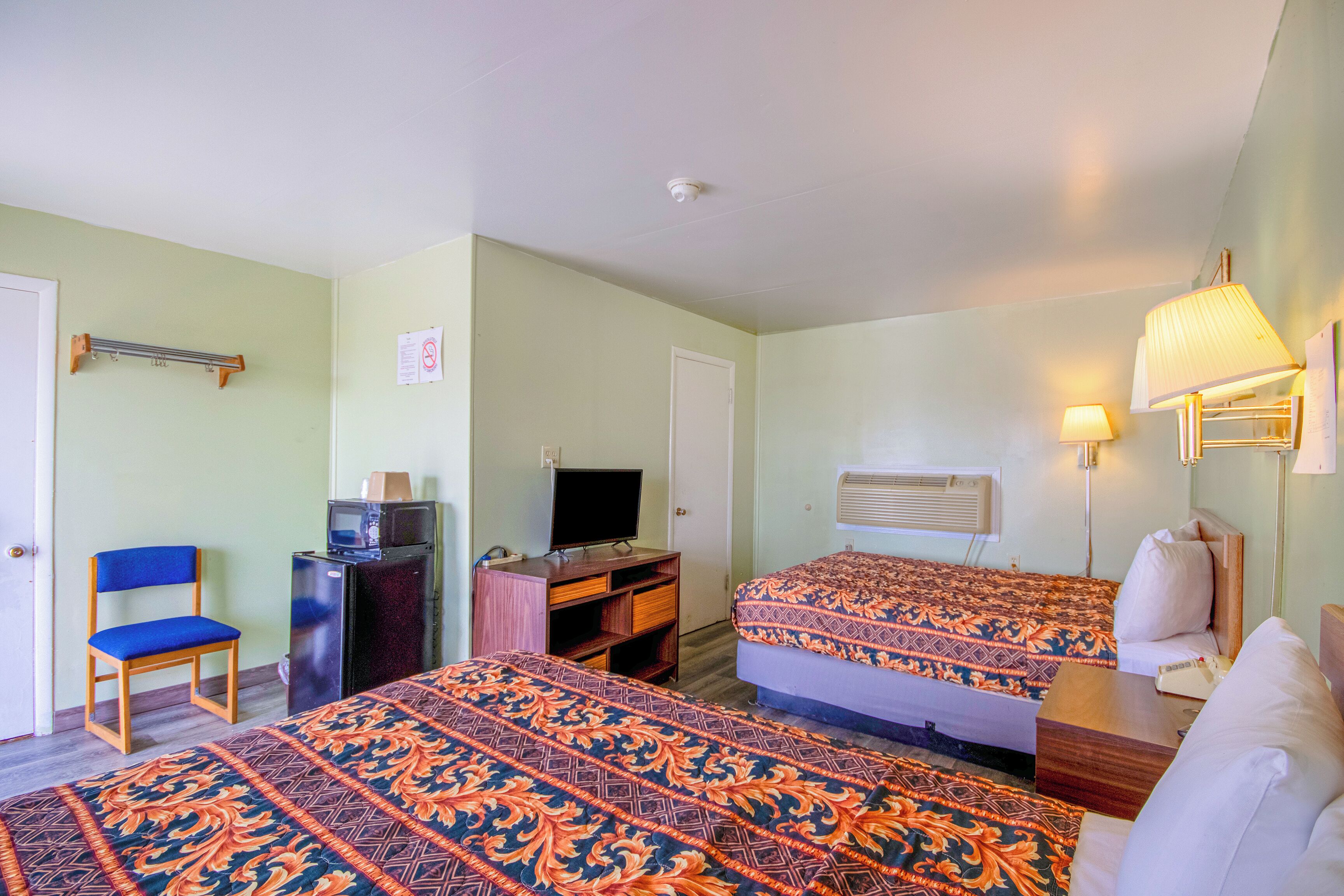A hotel room with two beds, a desk with a television, a chair, and a lamp.