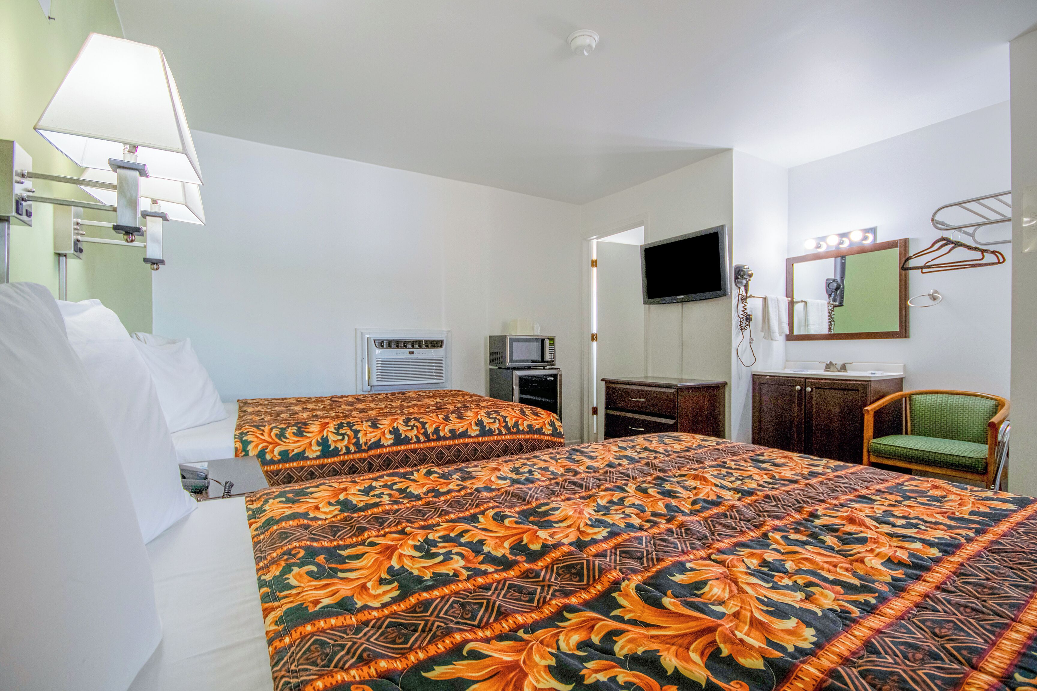 A hotel room with two beds, a television, a mirror, and a chair.