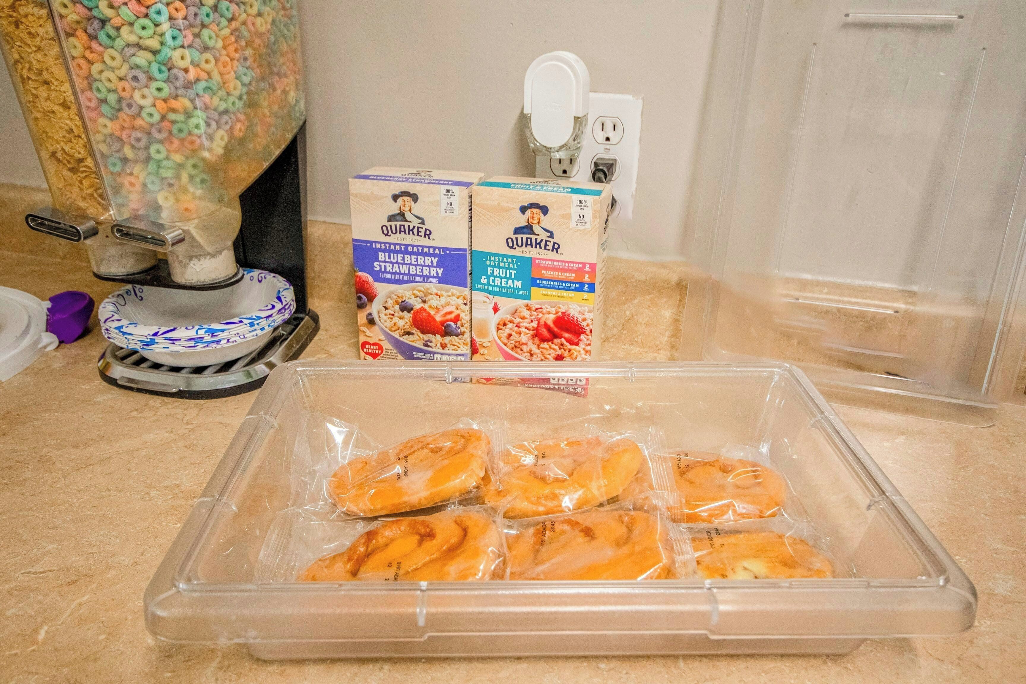 Un distributeur de céréales, des boîtes de céréales Quaker et un récipient en plastique contenant des pâtisseries, le tout posé sur un plan de travail de cuisine.
