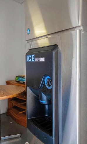 Dispensador de hielo de acero inoxidable con un botón azul que dice 'PUSH FOR ICE' en una cocina.