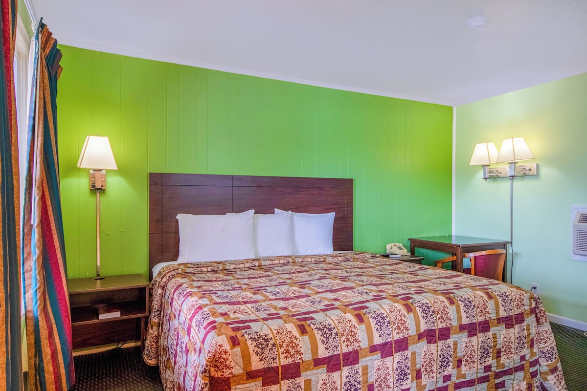 Quarto de hotel com uma cama grande, uma escrivaninha com cadeira e duas luminárias de parede.