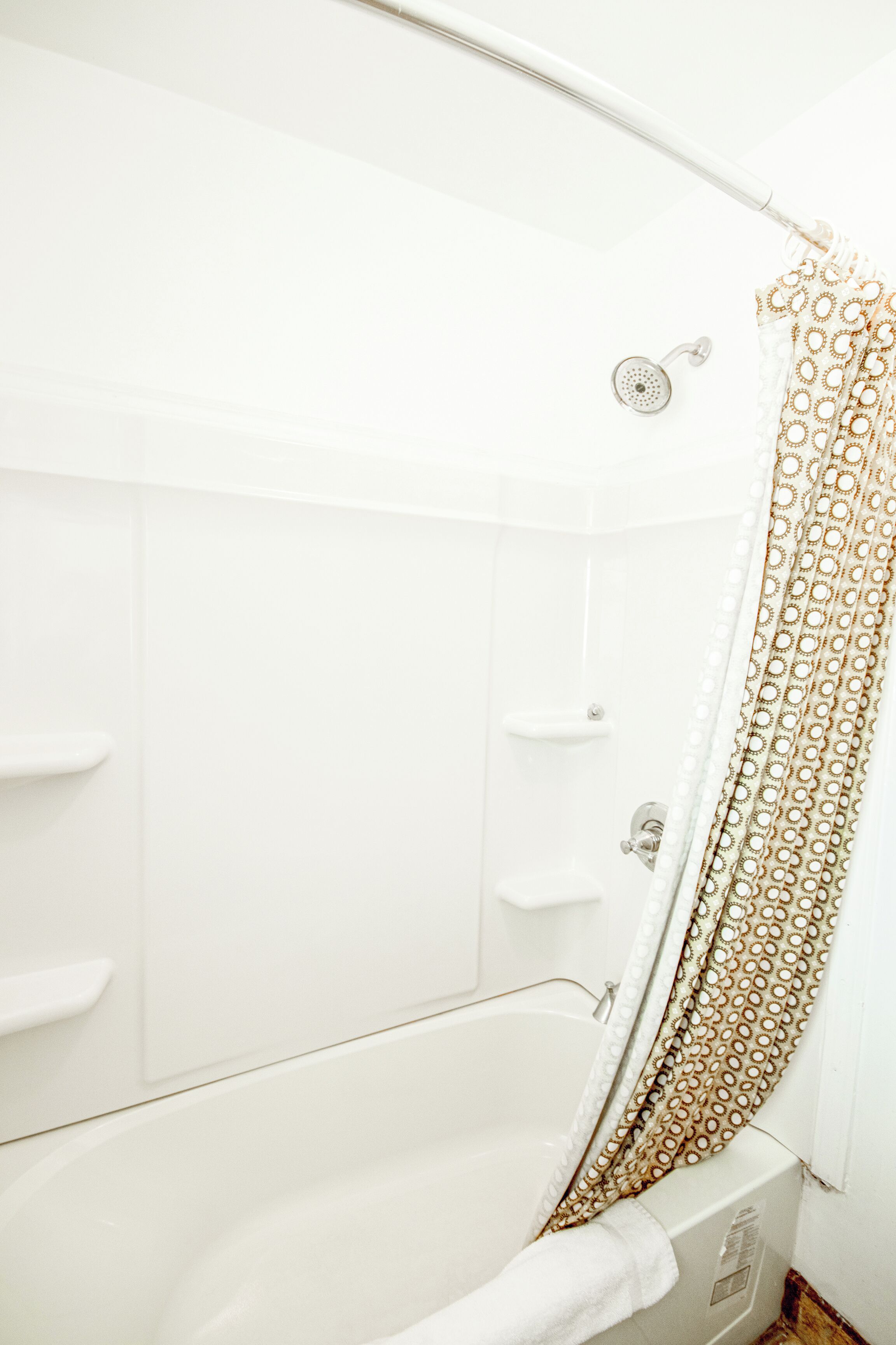 A white bathtub with a gold patterned shower curtain, a handheld showerhead, and a white towel.