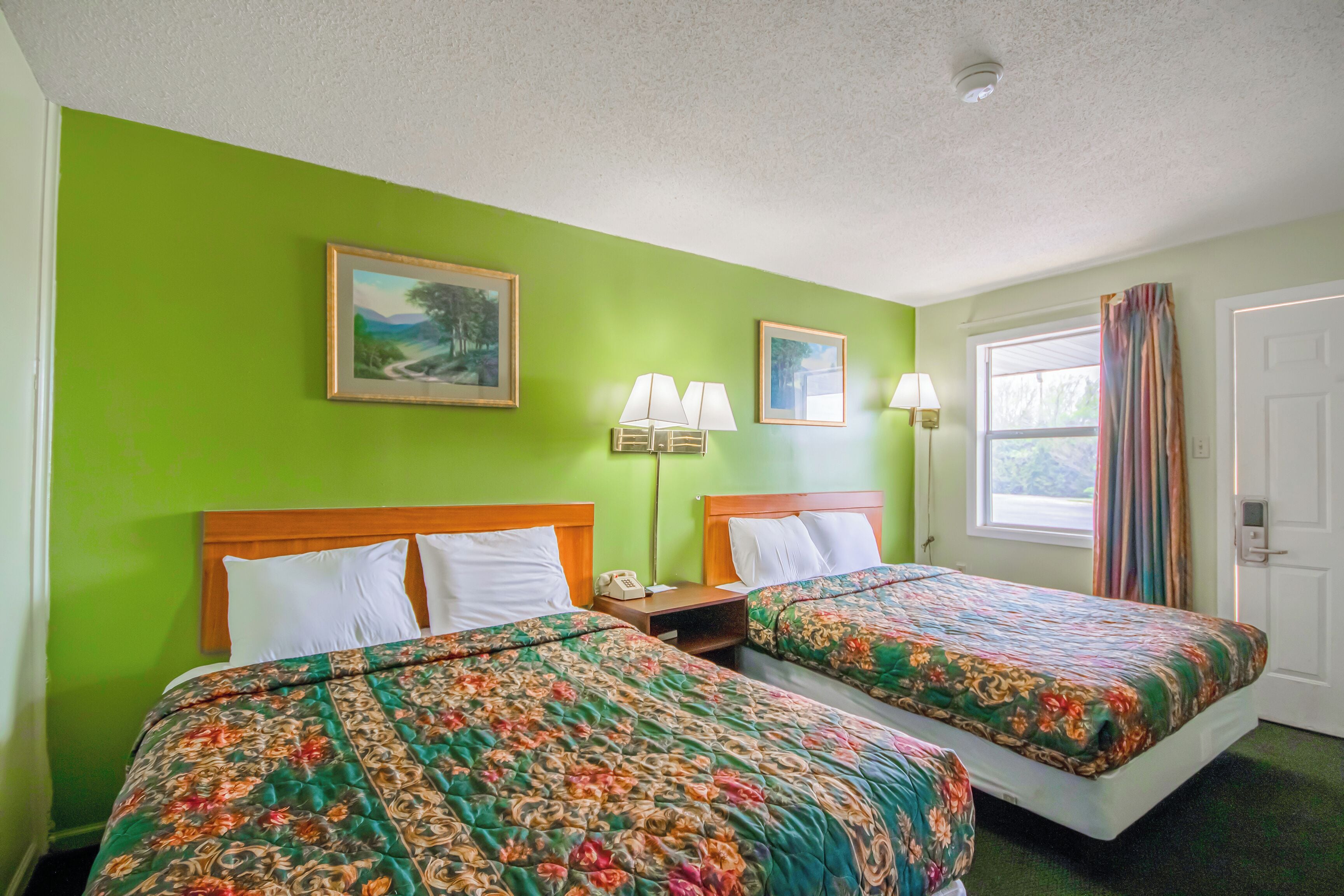 Habitación de hotel con dos camas, paredes verdes, una ventana con cortinas y una puerta.