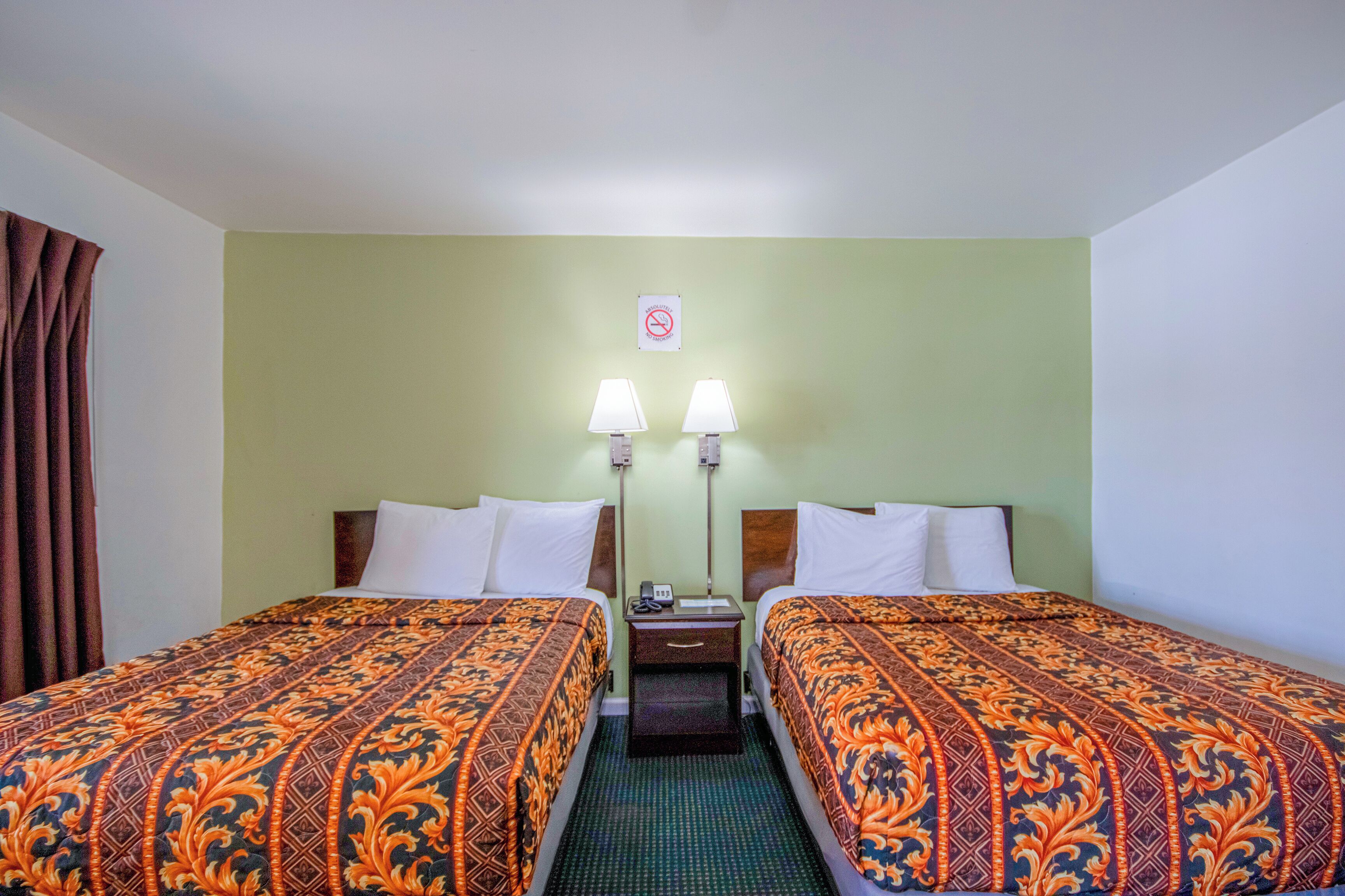 A hotel room with two beds, each with patterned bedding, a nightstand with a lamp, and a wall-mounted sign.