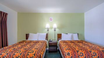 A hotel room with two beds, each with patterned bedding, a nightstand with a lamp, and a wall-mounted sign.