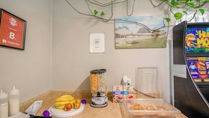 A kitchen counter with fruits, a blender, and a refrigerator with a game display.