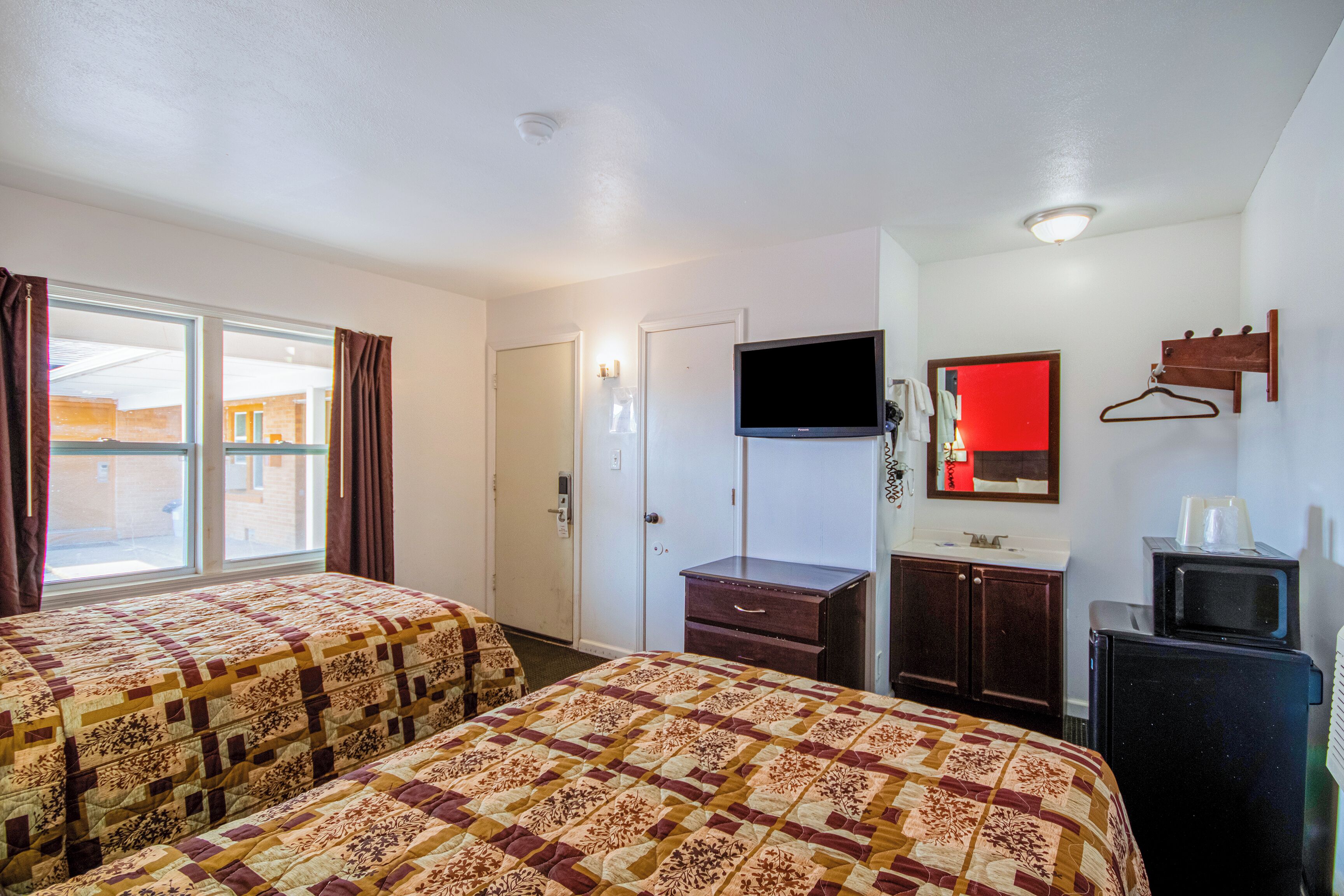 Ett hotellrum med två sängar, en tv, en byrå och en spegel.
