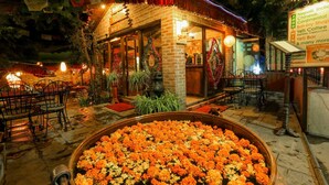 A cozy restaurant with a brick exterior, outdoor seating, and a large flower arrangement in the foreground. - Hotel Manang (Kathmandu)