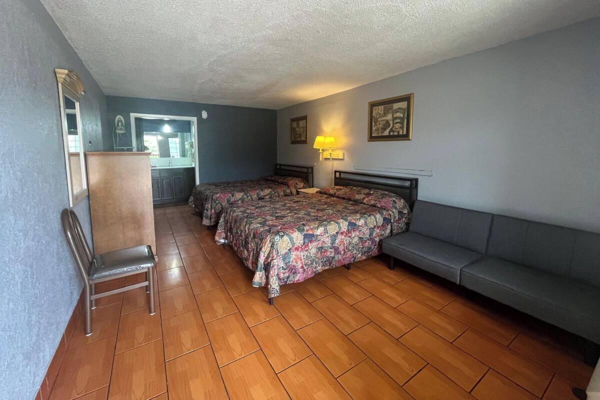 A room with two beds, a chair, a sofa, a desk, and a mirror.