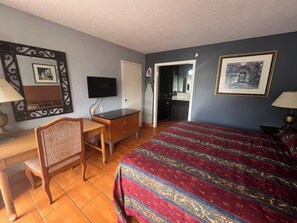 Een hotelkamer met een bed, een bureau, een stoel, een televisie en een deur naar een badkamer.