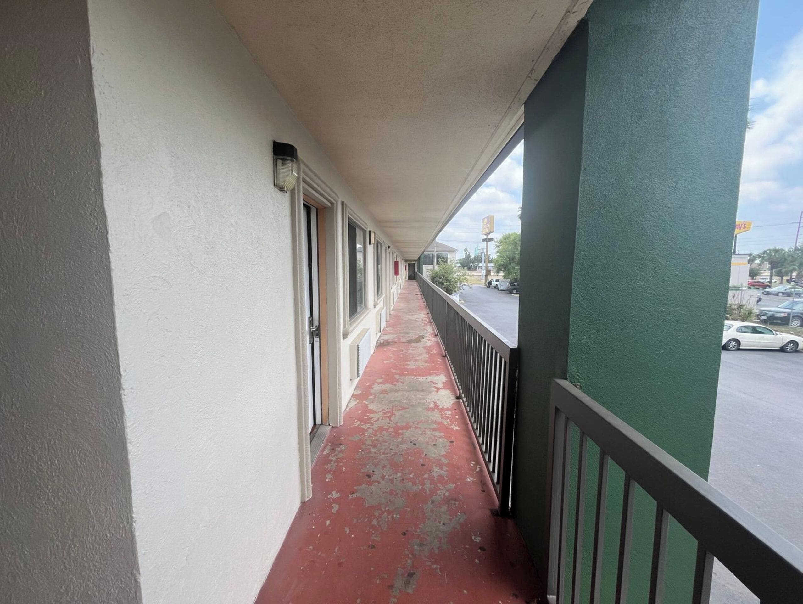 A narrow corridor with a red floor, white walls, and a green column on the right.