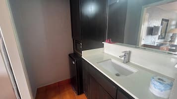 A bathroom with a white sink, dark cabinets, a black microwave, and a mirror above the sink.