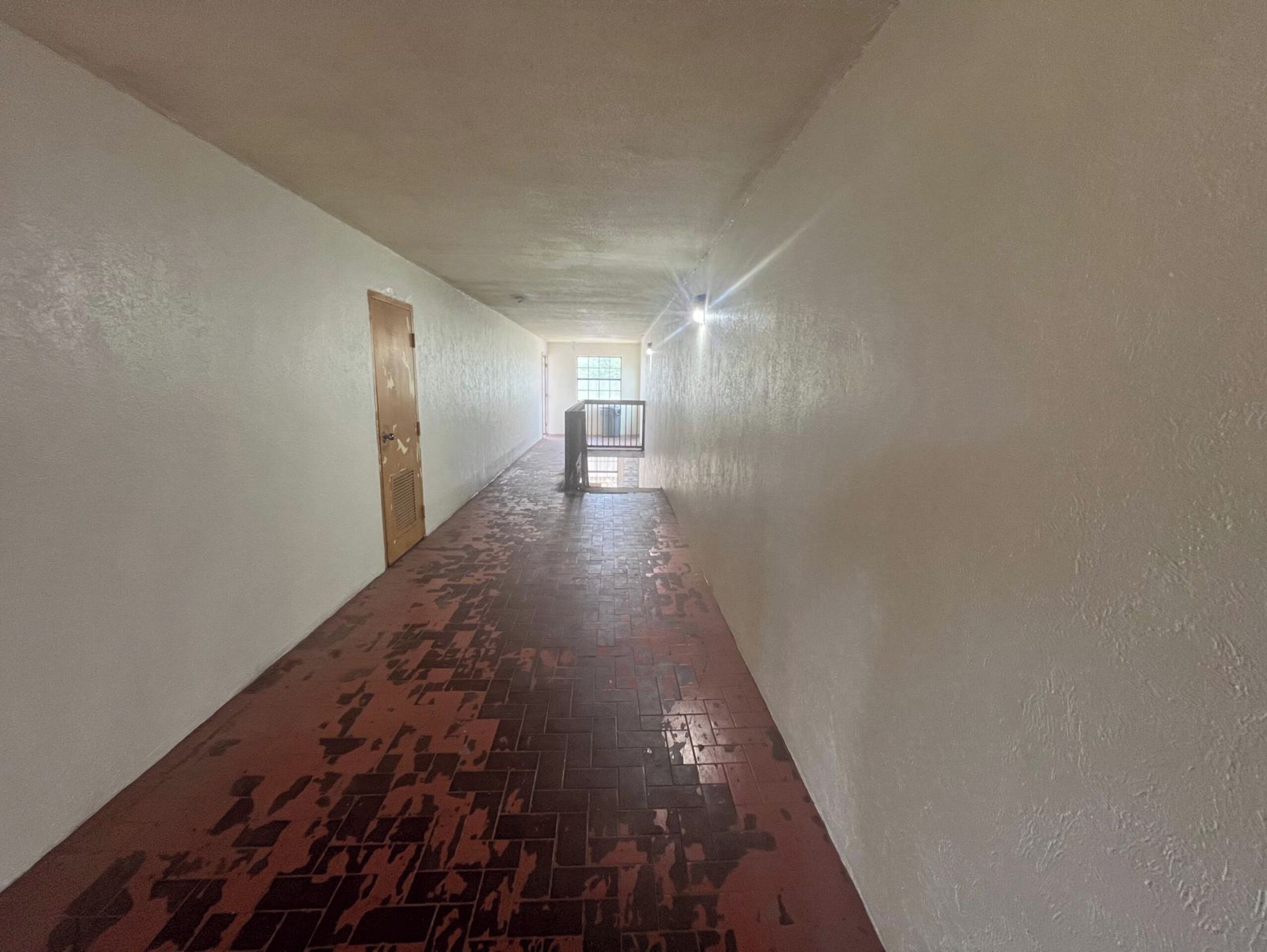 Un long couloir étroit, doté d’un sol carrelé et de murs sobres.
