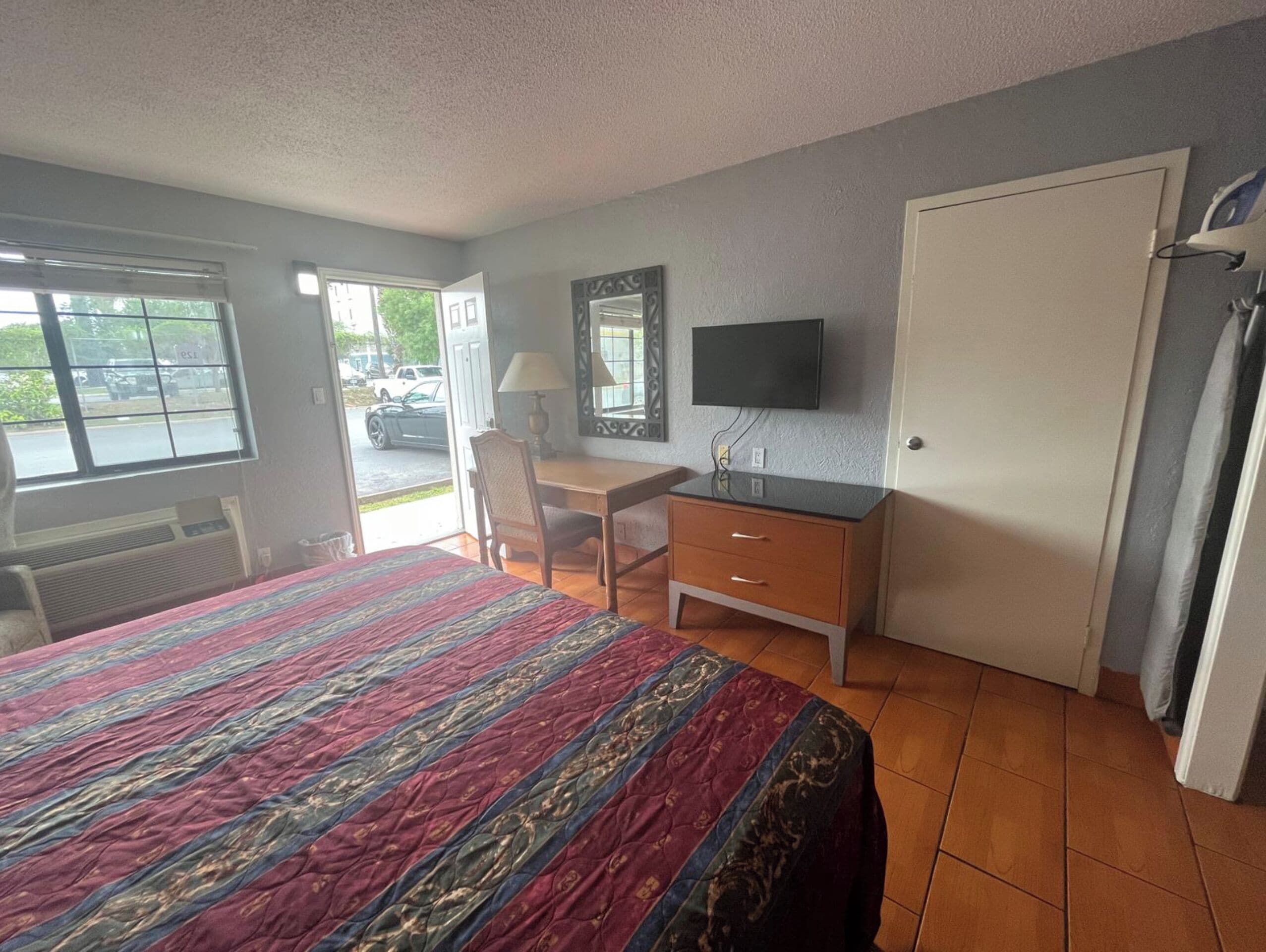 Habitación de hotel con cama, escritorio, silla, televisor y puerta.