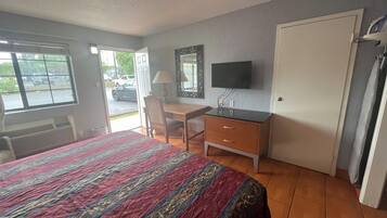 Habitación de hotel con cama, escritorio, silla, televisor y puerta.
