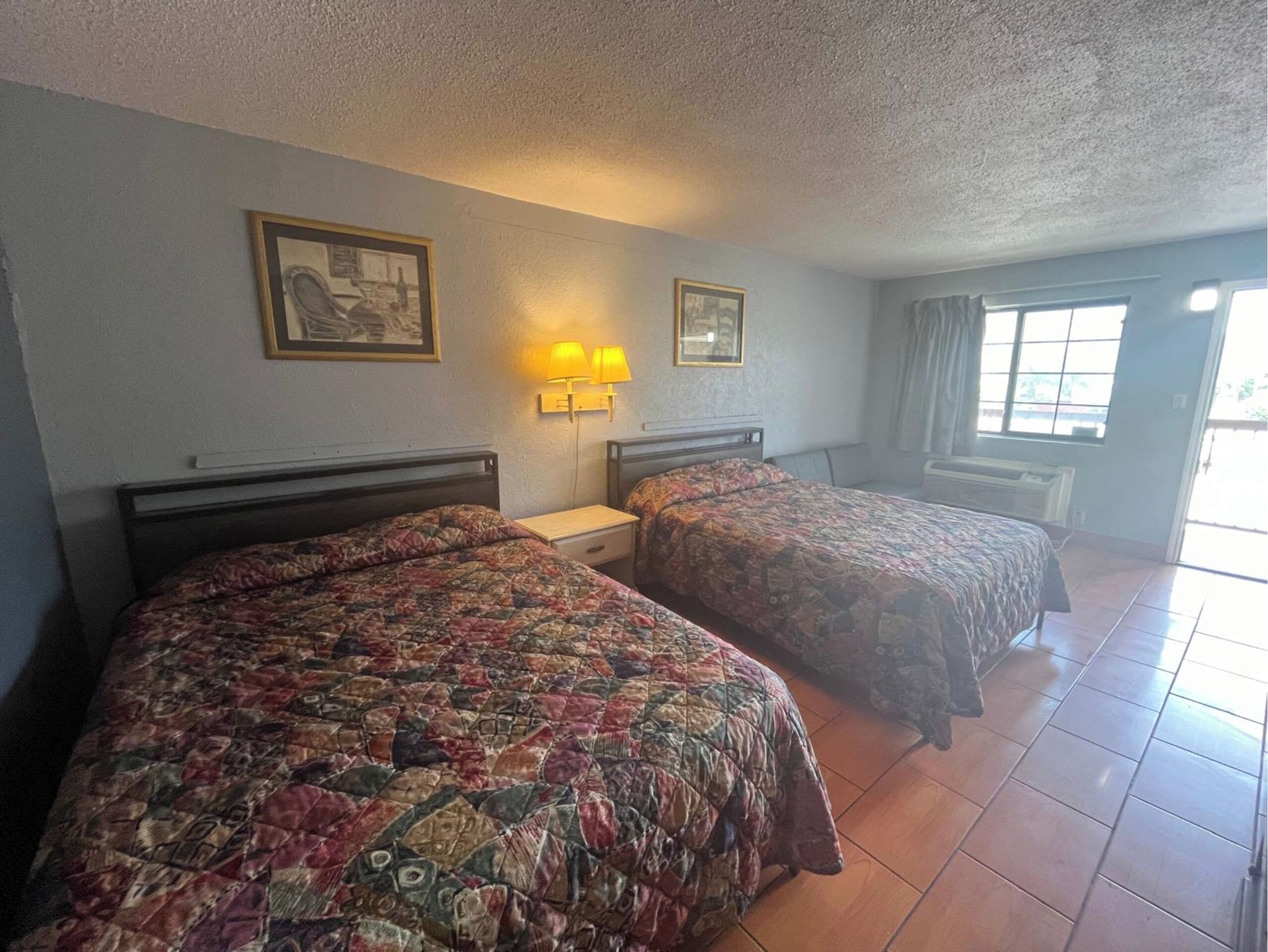 A room with two beds, a nightstand, wall-mounted lamps, and framed pictures.