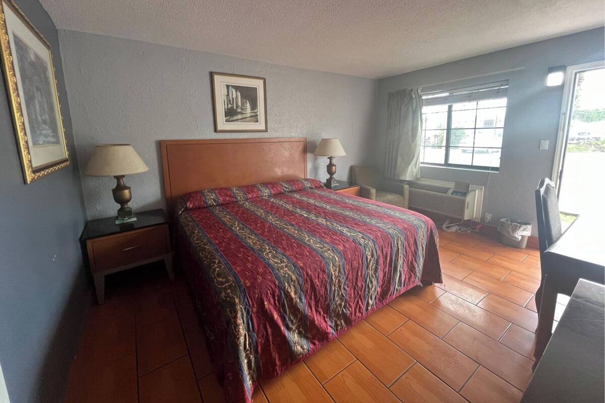 A hotel room with a wooden bed, two bedside tables with lamps, a framed picture on the wall, and a window with curtains.