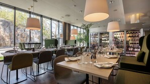 A restaurant with tables set for dining, a bar area with wine bottles, and large windows offering a view of the outdoors.
