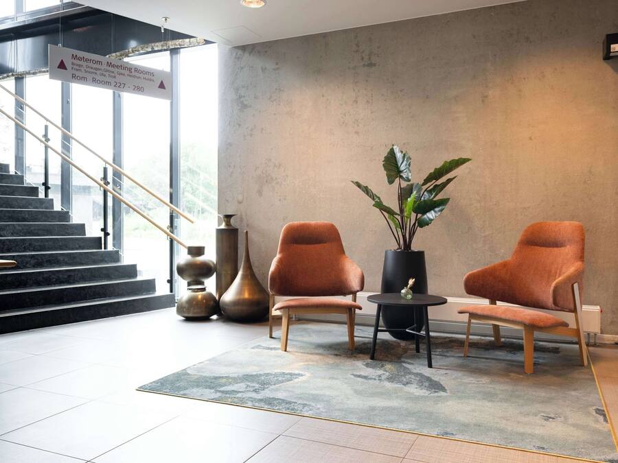 Un hall d’entrée moderne avec un escalier, deux fauteuils orange, une plante en pot et un panneau indiquant l’emplacement des salles de réunion.