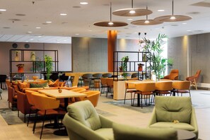 A modern indoor space with multiple seating areas, including tables and chairs, and shelves with plants.