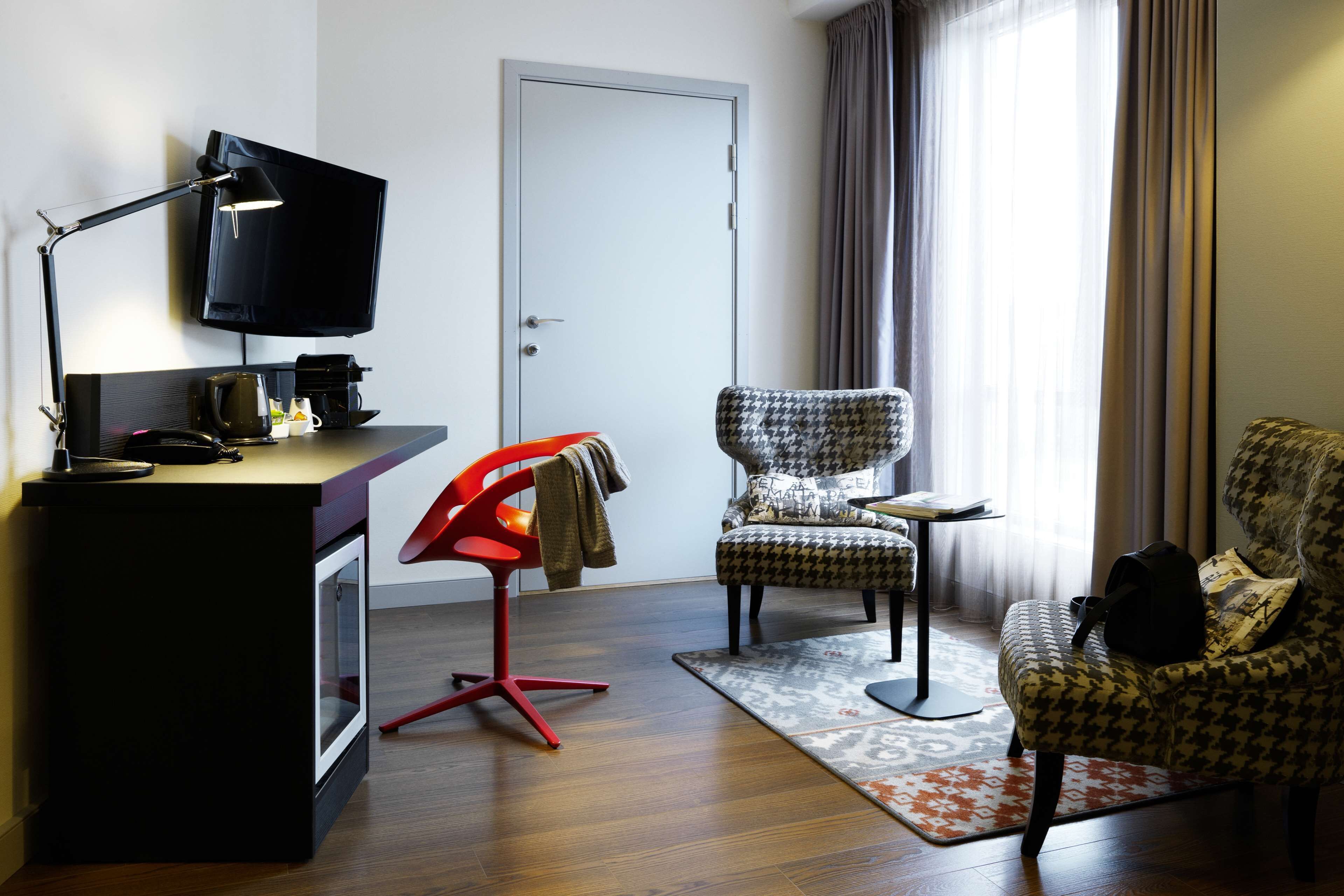 Een moderne hotelkamer met een bureau, een televisie, een rode stoel, een gestreept fauteuil en een bank.