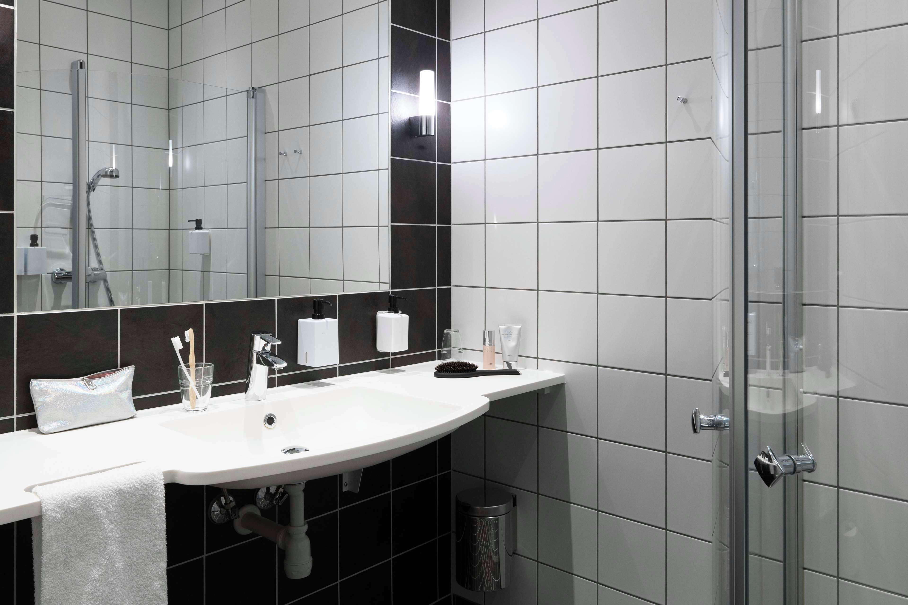Ett modernt badrum med en vit tvättställ, spegel och duschavdelning med glasväggar.