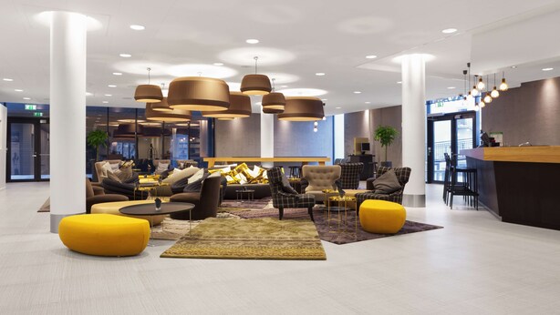 A modern lobby with multiple seating areas, a reception desk, and a large window providing a view of the city.