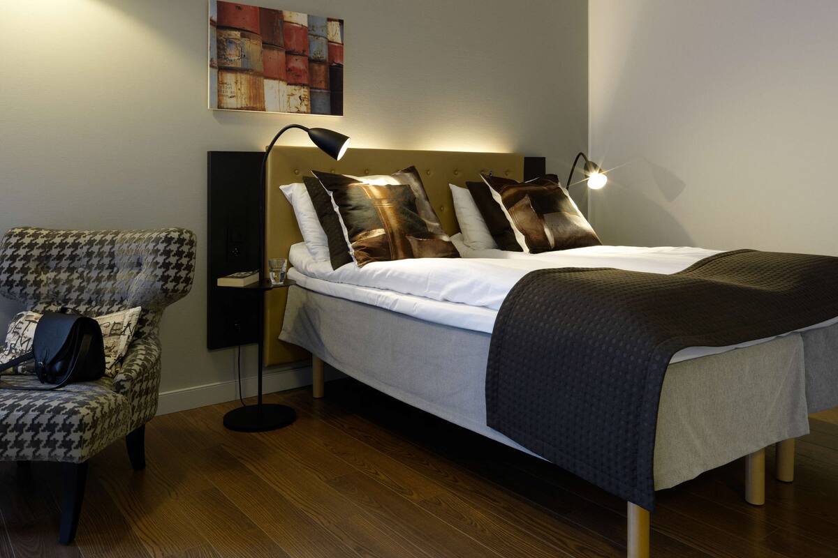 A neatly arranged bedroom with a bed, a chair, a bedside table, and a floor lamp.