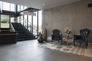 Een hal met een trap, een receptiebalie, twee fauteuils, een vaas met bloemen en een grote vaas.