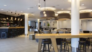 A modern bar area with a long wooden counter, multiple stools, and hanging pendant lights.