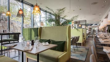 Un restaurante moderno con asientos verdes, ventanas amplias e iluminación colgante.