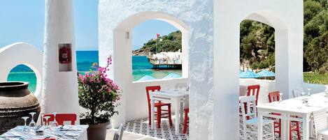 A seaside restaurant with white and blue architecture, outdoor seating, and a view of the sea.