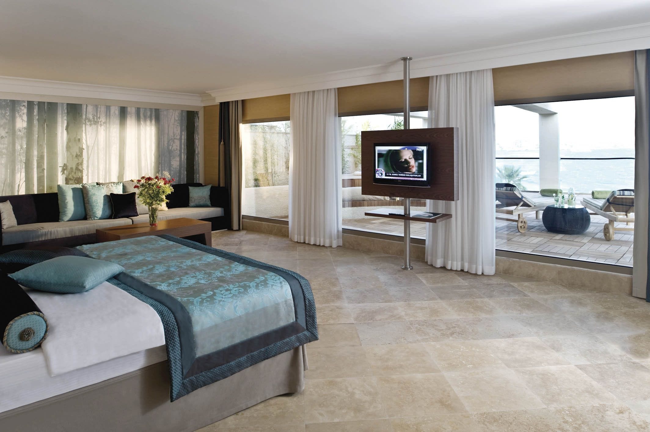 Un dormitorio amplio con una cama grande, televisión y un balcón con mobiliario de exterior.