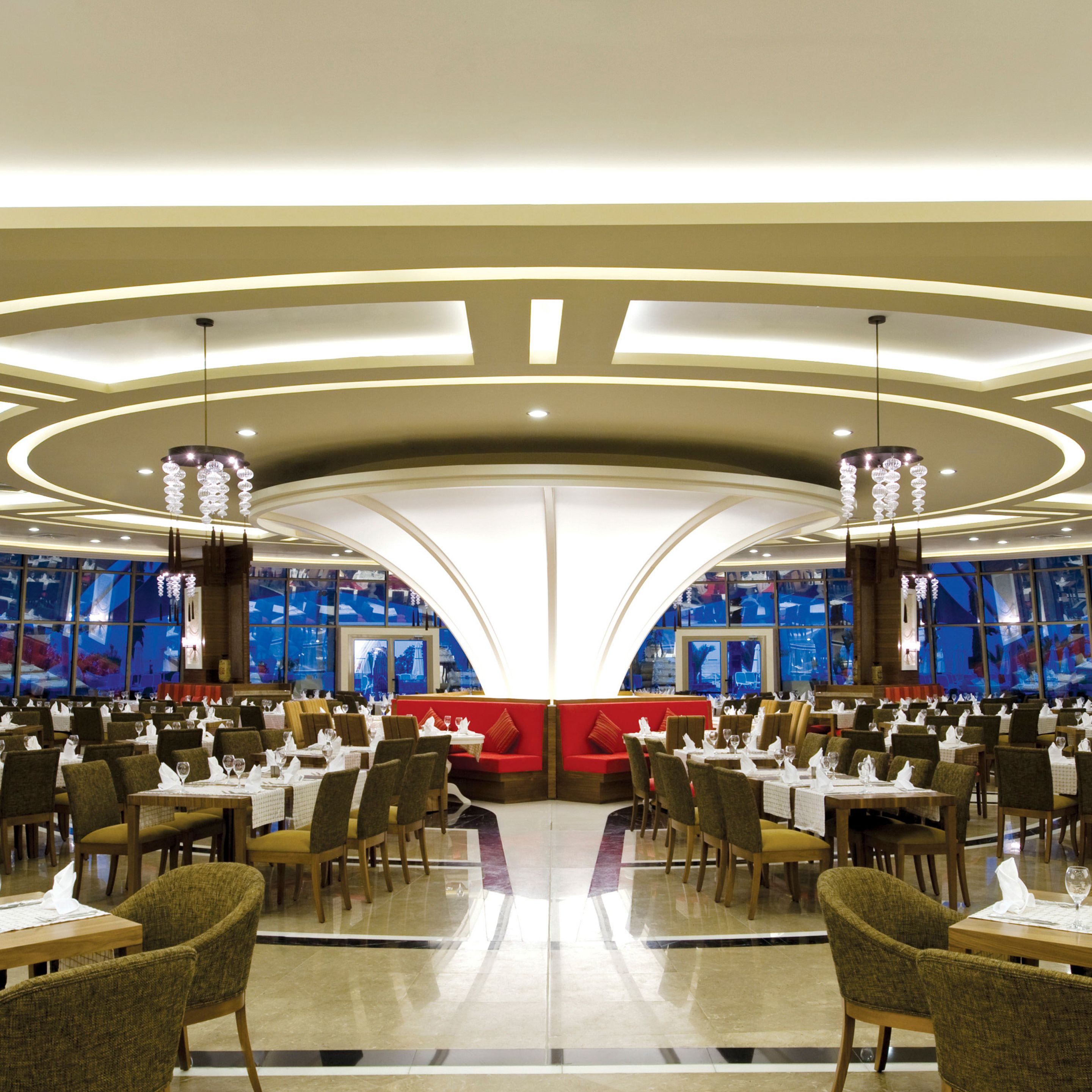 Um restaurante amplo com um assento central vermelho, várias mesas de jantar e um design de teto moderno.