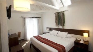 Habitación de hotel con una cama grande, un escritorio, una silla, una mesita de noche con lámpara y un teléfono instalado en la pared.
