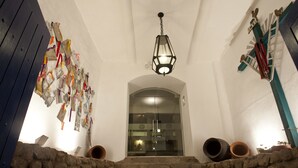 Una escalera conduce a una habitación con puerta de cristal, rodeada de muros de piedra y un farol colgante.