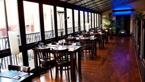 Un restaurant avec des tables et des chaises en bois, de grandes fenêtres et un couloir éclairé de lumière bleue.
