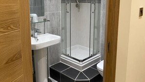 Une salle de bain moderne avec une douche à parois de verre, un lavabo sur colonne blanc et un sol carrelé.