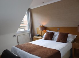 A hotel room with a bed, a nightstand, a lamp, and a view of the outside.