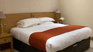 Ein ordentlich bezogenes Bett mit weißen Leinen und einem braunen Akzent, ein Nachttisch aus Holz mit einer Lampe und eine Vase mit Blumen daneben.