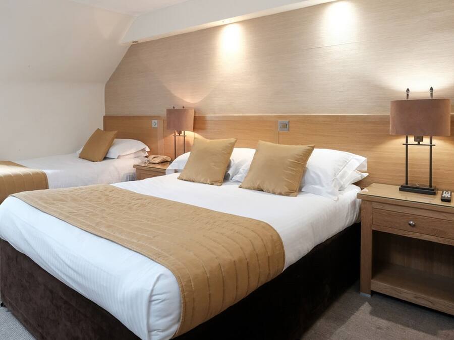 Una habitación de hotel con dos camas, cabeceros de madera, lámparas de noche y una mesita de noche con cajón.