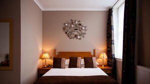 Un lit bien fait, recouvert d’une couverture marron, avec deux lampes de chevet et un élément décoratif fixé au mur.